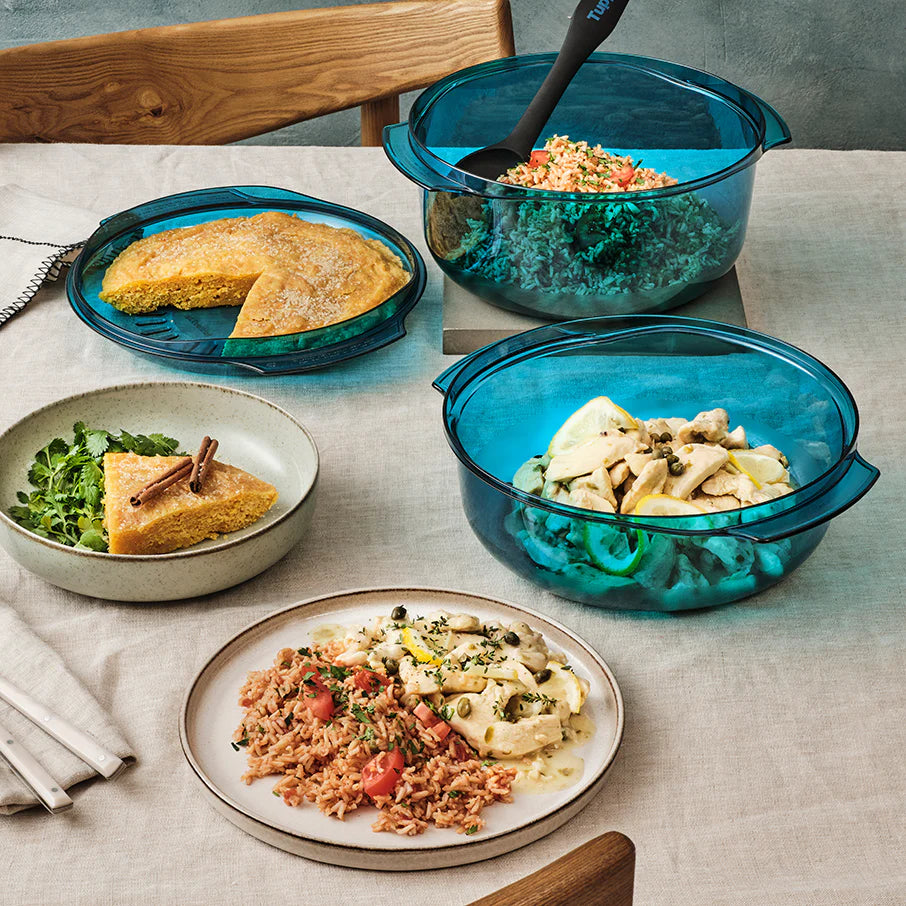 Dishes of food on a table with blue Tupperware dishes and plates.